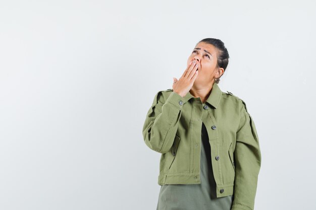 Woman yawning while looking up in jacket, t-shirt and looking sleepy
