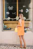 Free photo woman in yellow dress in front of jewelry store