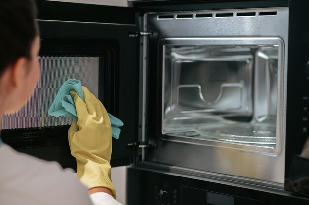 A woman in yellow gloves cleaning the oven