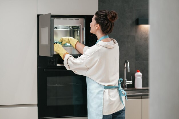 Женщина в желтых перчатках чистит духовку