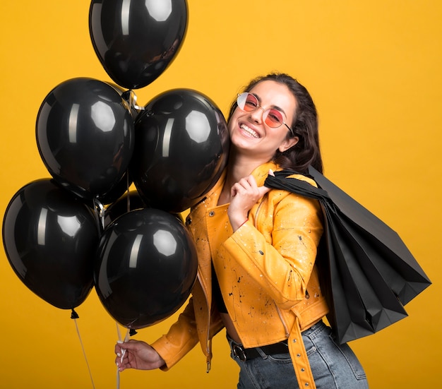 Free photo woman in yellow jacket holding black friday balloons