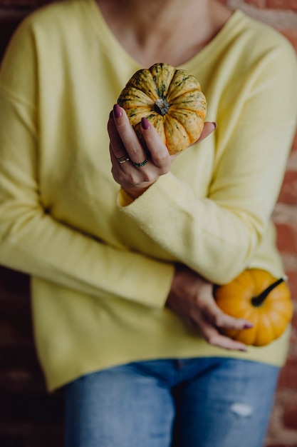 Free photo woman in a yellow sweater holding pumpkins in her hands