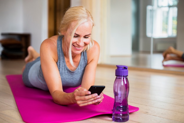 Женщина на коврик для йоги, проверка ее телефон