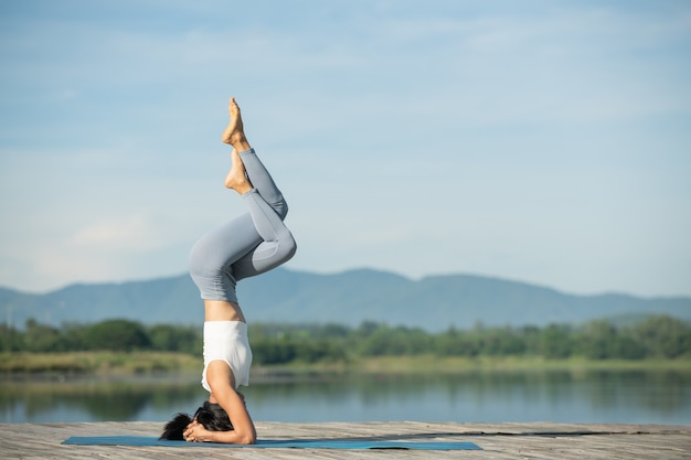 공원에서 휴식을 요가 매트에 여자. 요가 연습, headstand 운동을 하 고, 운동, 운동복, 바지와 탑을 입고 젊은 스포티 한 아시아 여자.