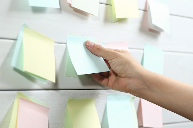 Womans hand sticking notepapers on white wooden board