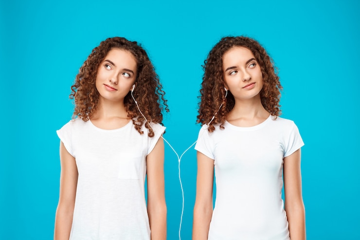 Free Photo womans twins listening music in headphones, smiling over blue.