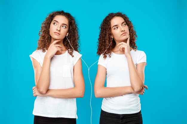 womans twins listening music in headphones, thinking over blue.