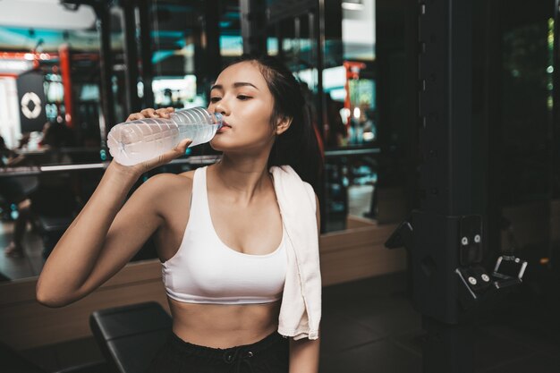 Women after exercise drink water from bottles and handkerchiefs in the gym.