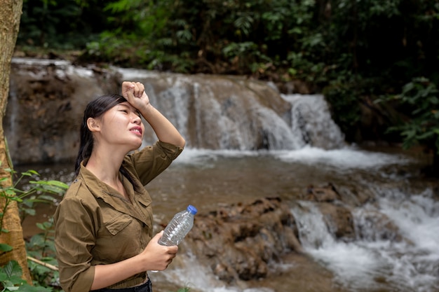 女性は森の中で新鮮な水を飲んでハイキングしています