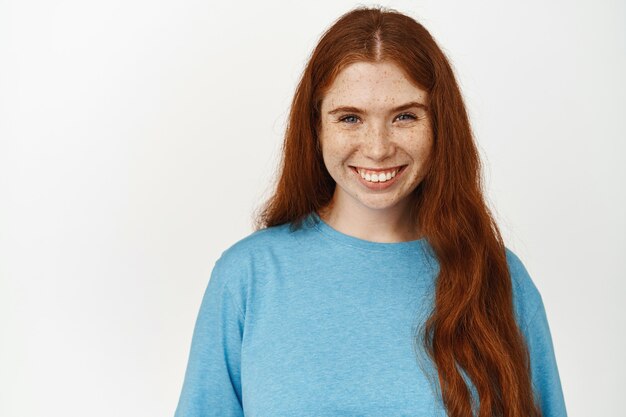 Women beauty. Close up shot of smiling natural girl with long red hair on white.
