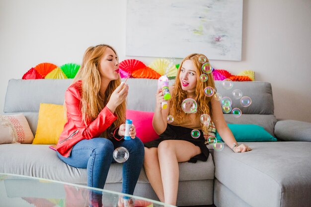 Women blowing bubbles on sofa