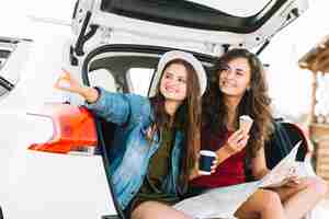 Free photo women on car trunk with map looking away