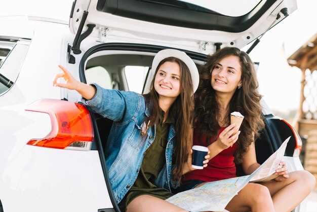 Women on car trunk with map looking away 