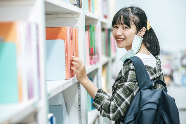 バックパックを背負って図書館で本を探している女性。