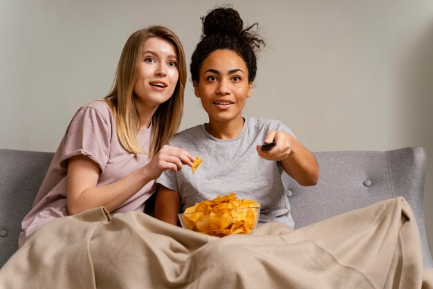 Women on couch watching tv and eating chips