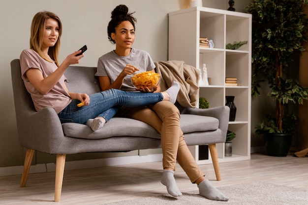 Donne sul divano a guardare la tv e mangiare patatine