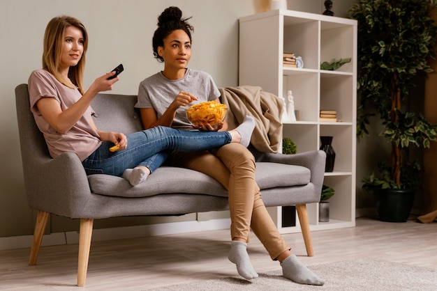 Women on couch watching tv and eating chips