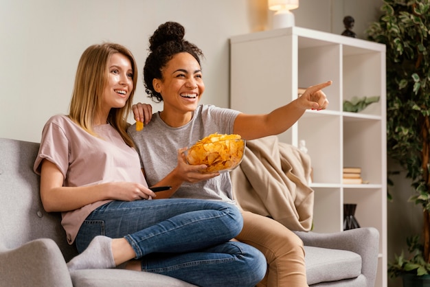 Women on couch watching tv and eating chips