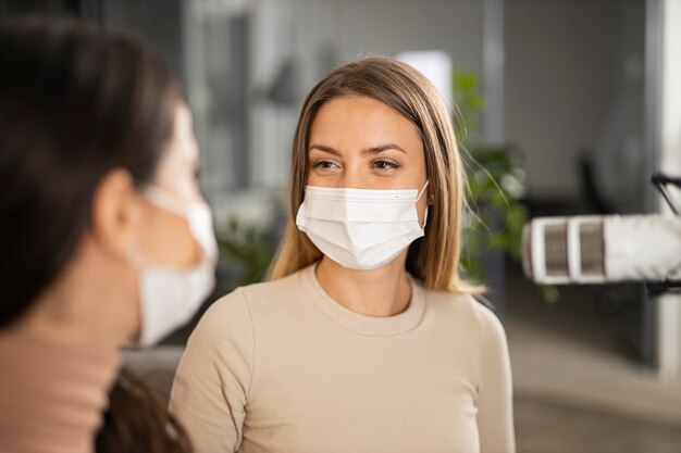 Women doing radio together while wearing medical masks