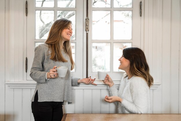 女性はコーヒーを飲み、窓の近くで話す