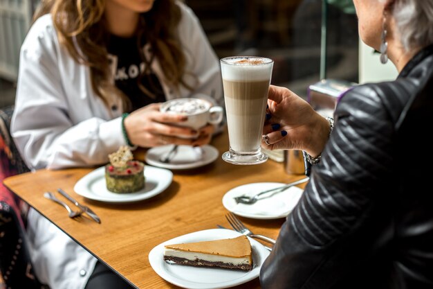 Women drinking coffee with desserts cheesecake and pistachios cake side view