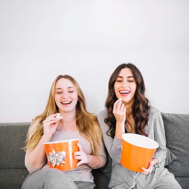 Women eating popcorn on sofa