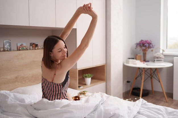 Free photo women enjoying coffee with marshmallows on the bed with present near her while stretching after awaking.