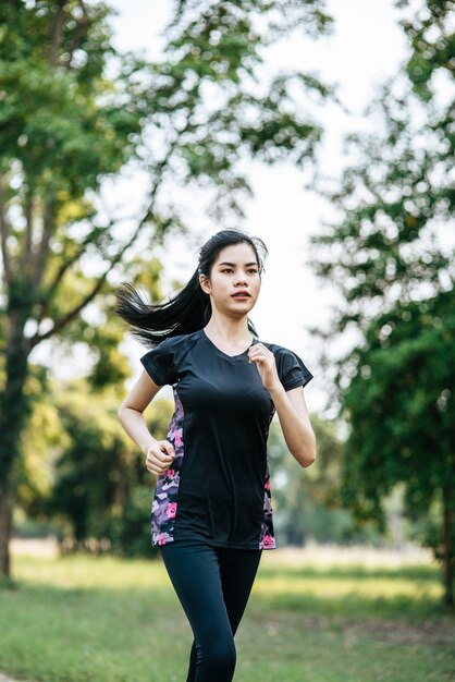 女性は公園の路上を走って運動します。