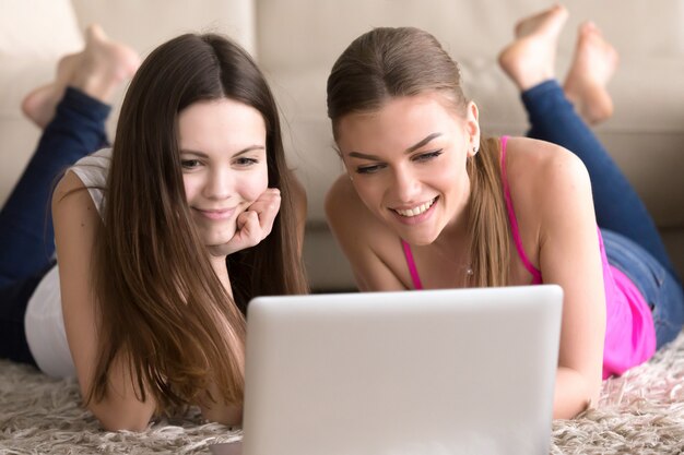 Women friends lying on floor in front of laptop