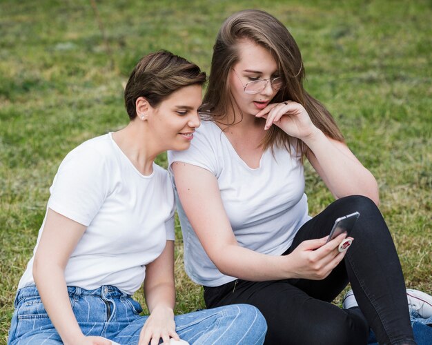 Женщины друзей, используя смартфон, сидя на траве