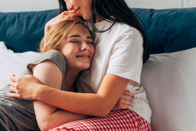 Women gently hugging smiling girlfriend in bed