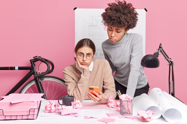 Бесплатное фото Женщины-графические дизайнеры, недовольные неудачей во время работы, позируют в коворкинге, используют современный смартфон