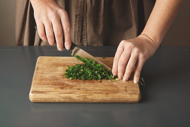 Women hand chop parsley on wooden board on old blue table.