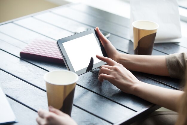 女性の手は、カフェで白い空の画面とタブレットを持っています。閉じる