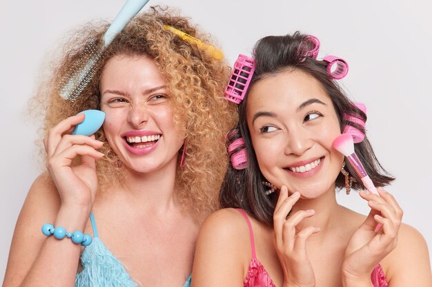 女性は幸せな表情を持っているファンデーションを適用する化粧品のツールを使用して髪型をパーティーウェアの準備をする白で隔離されたファッショナブルなドレス