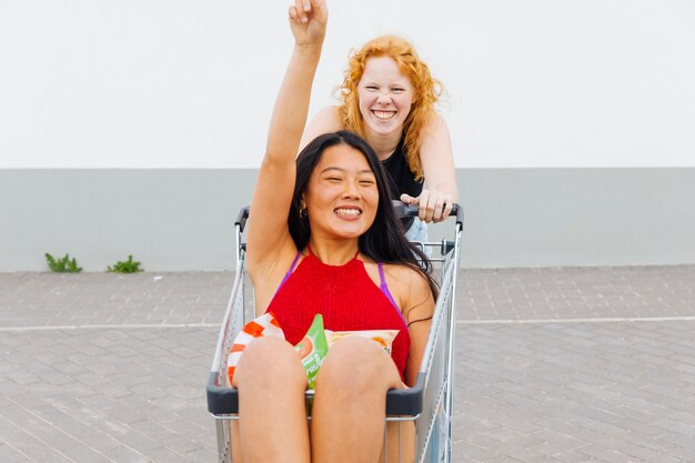 Women having fun with shopping trolley and looking at camera 