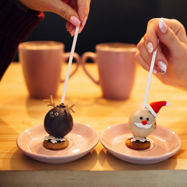 Women hold sticks with sweets in Christmas design on pink plates