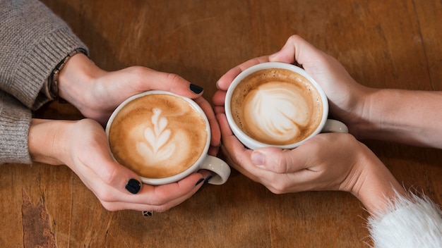 Women holding cups of coffee on table 