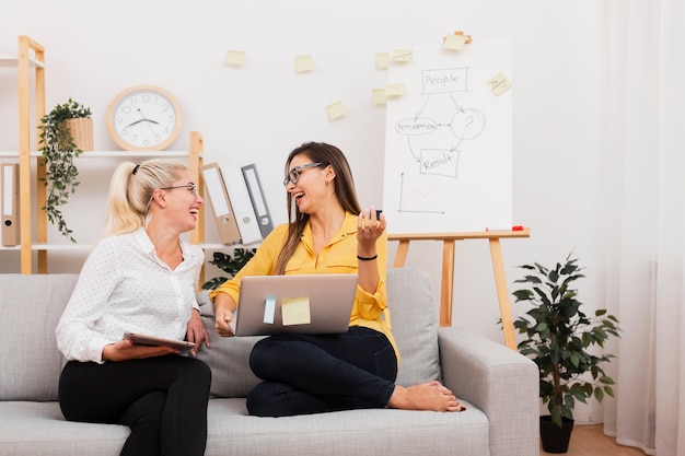 Women holding gadgets and sitting on sofa