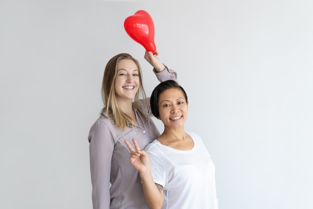 Women holding heart shaped balloon and showing victory sign