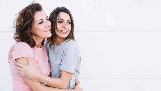 Women hugging near white wall