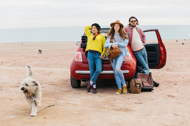 女性と車とビーチを走る犬の近くの男