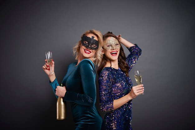 Women in masks drinking champagne in studio shot