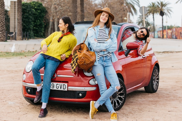 Foto gratuita le donne si avvicinano all'uomo sporgendosi dalla macchina e mostrando pollice in su