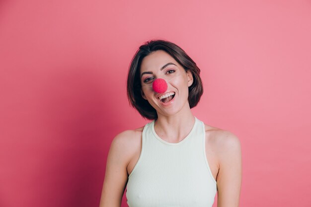 Women on pink background pretty funny and smiling young woman wearing clown nose, party mood