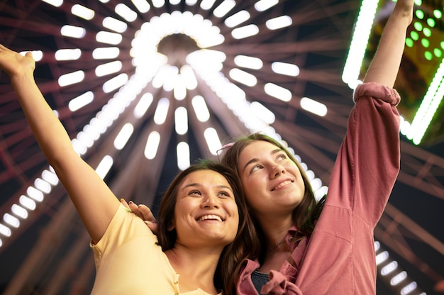 Foto gratuita donne in posa al parco di divertimenti accanto alla grande ruota