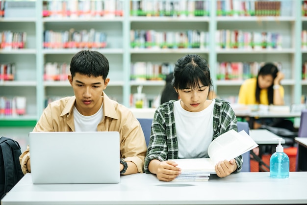 Women read books and men use laptops to search for books in libraries.