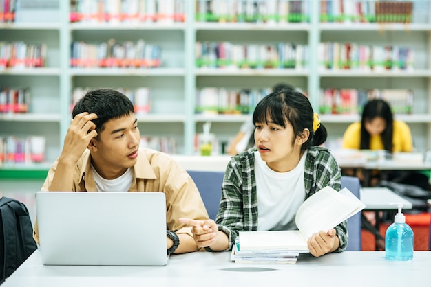 Women read books and men use laptops to search for books in libraries.