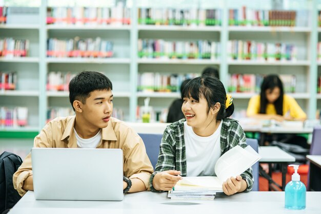 Women read books and men use laptops to search for books in libraries.