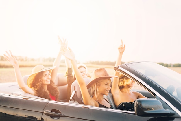 Free photo women riding car with hands up